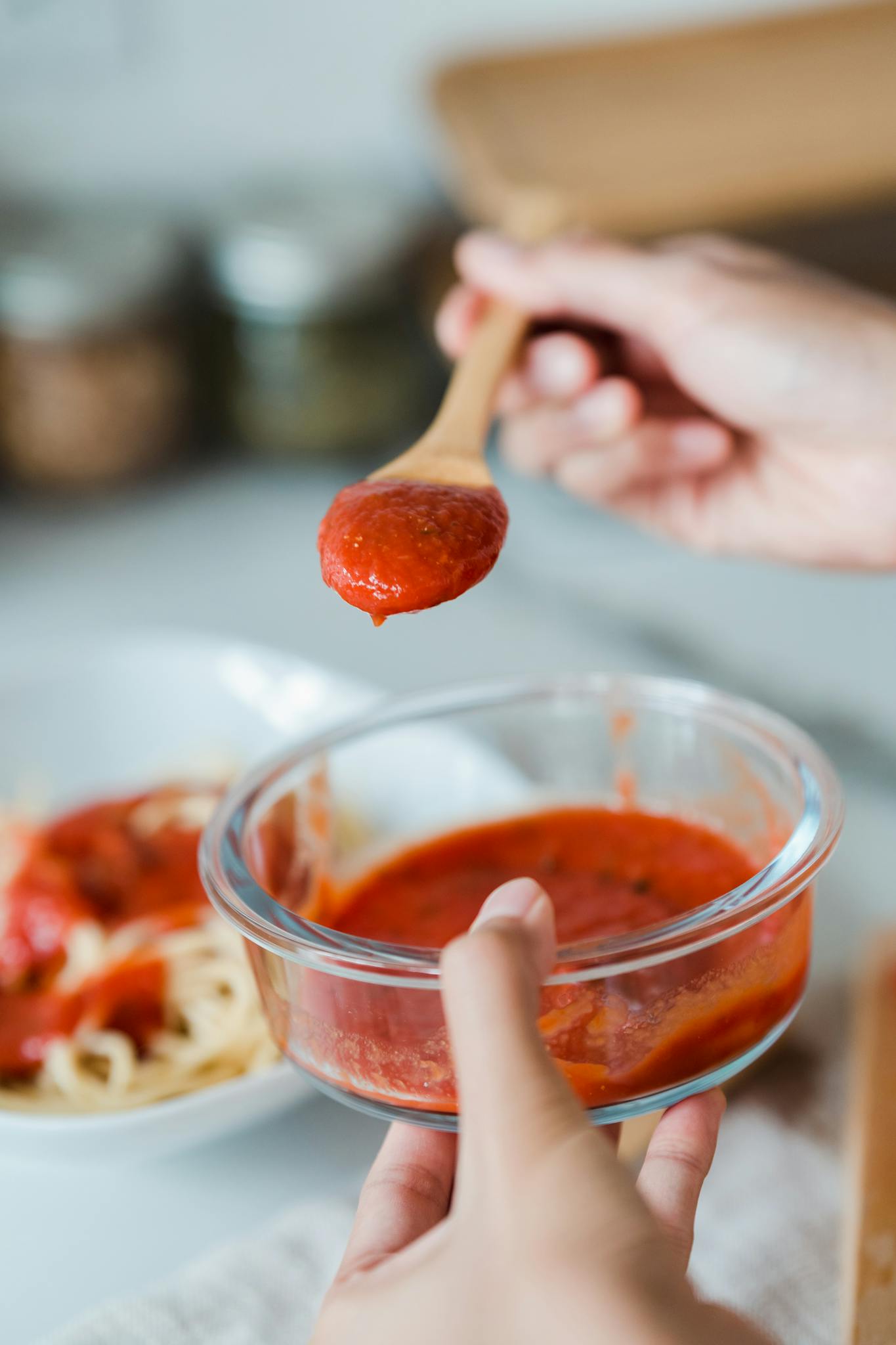 A hand pours tomato sauce from a wooden spoon into a bowl, perfect for cooking-themed imagery.