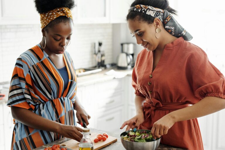 Two women in a modern kitchen preparing a fresh salad together. Vibrant and stylish setting.